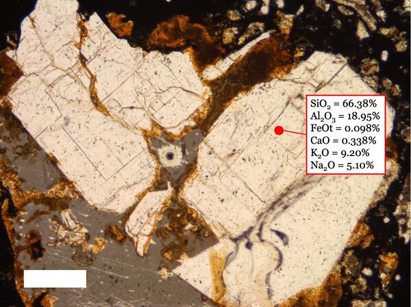Microscope view of beige irregular and broken crystal surrounded by gray material. Chemical composition given for one point.