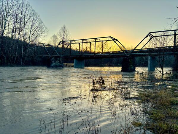 The sun rises behind a bridge spanning the Cowpasture River.