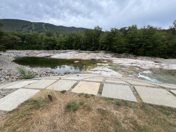 Low lying water in a river with a ski resort in the background during the summer.