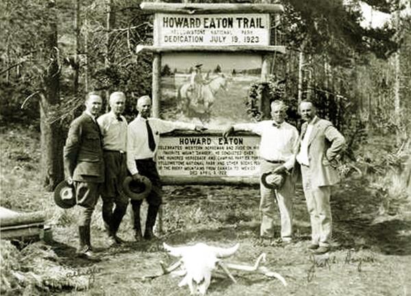 Five men in 1920s-era suits stand in front of a wooden sign for Howard Eaton Trail; forest behind and bison skull in front