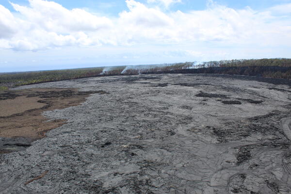 Color photograph of recent lava flows on crater floor with wildfire smoke in the background