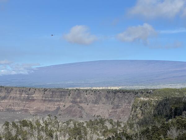 Color photograph of shield volcano with caldera wall in the foreground