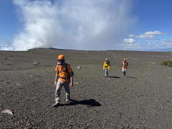 Color photograph of scientists walking across a new geologic deposit wearing safety gear