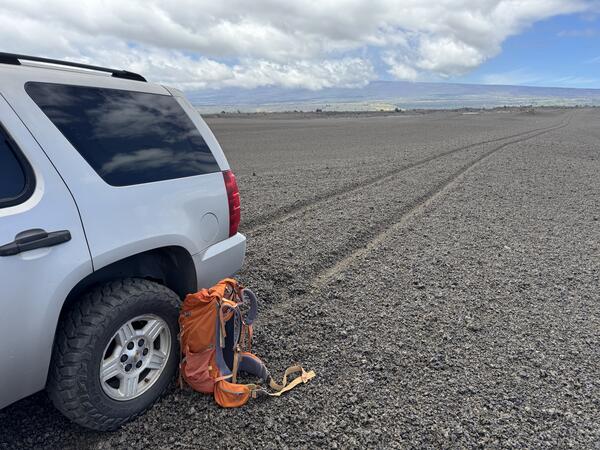 Color photograph of vehicle on volcanic terrain with tire tracks in the background