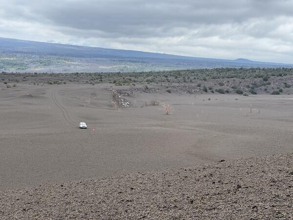 Color photograph of volcanic landscape with car driving in the distance