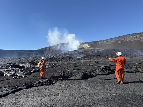 Color photograph of scientists in orange flight suits on a volcanic landscape