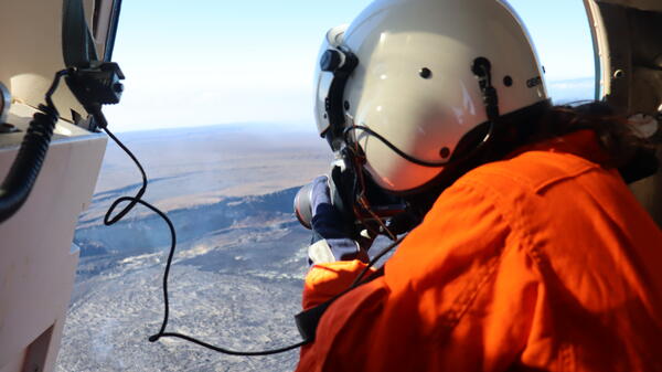 Color photograph of scientist in helicopter photo-documenting volcanic eruption