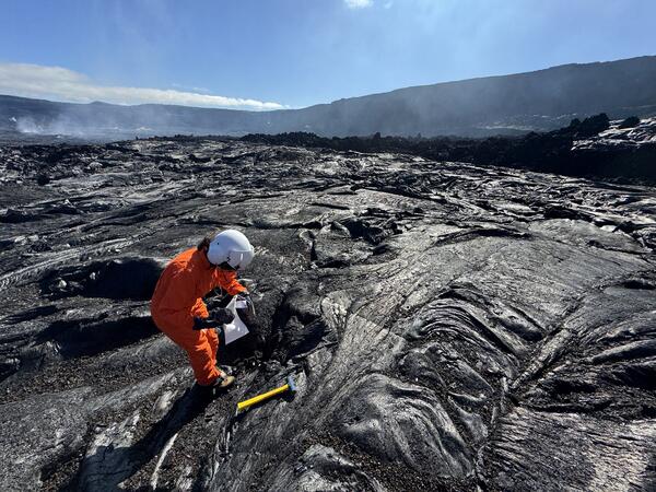Color photograph of scientist collecting sample of cooled and solidified lava from a recent eruption 