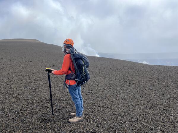 Color photograph of scientist wearing personal protective equipment and taking a measurement on a crater rim