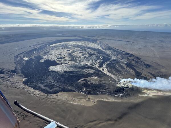 Color photograph of caldera at summit of volcano with gas plume from eruptive vents