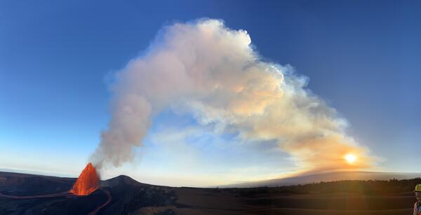 Color photograph of lava fountain and volcanic plume at sunset