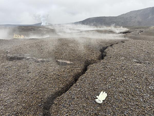 Color photograph of steaming ground crack with glove for scale