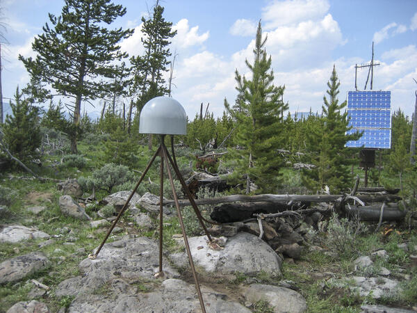 GPS antenna and solar panel in a lightly wooded area under partly cloudy skies