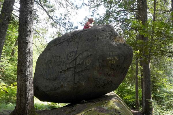 Person on sitting on top of a car-sized boulder perched on bedrock