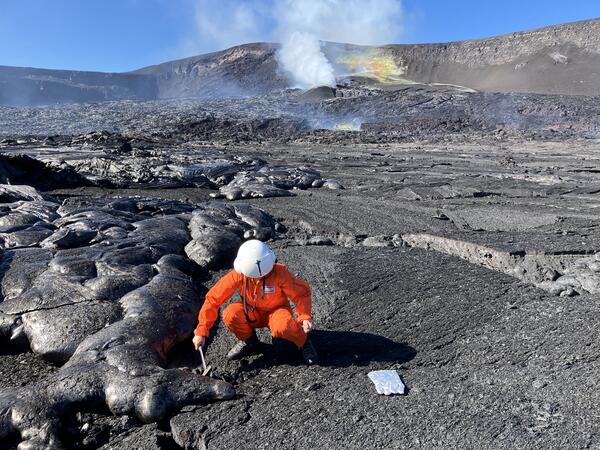 Color photograph of scientist collecting sample of cooled lava flow
