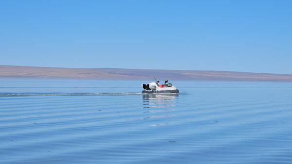 researchers on a hovercraft in the middle of Lake Abert, the lake is blue with brown foothills in the distant background