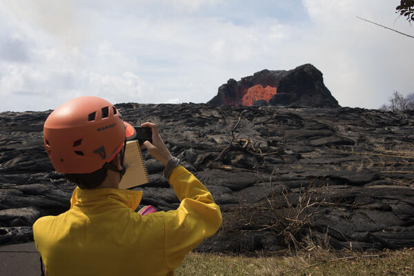 Scientist photographs bright orange lava flowing out of a cone of rock