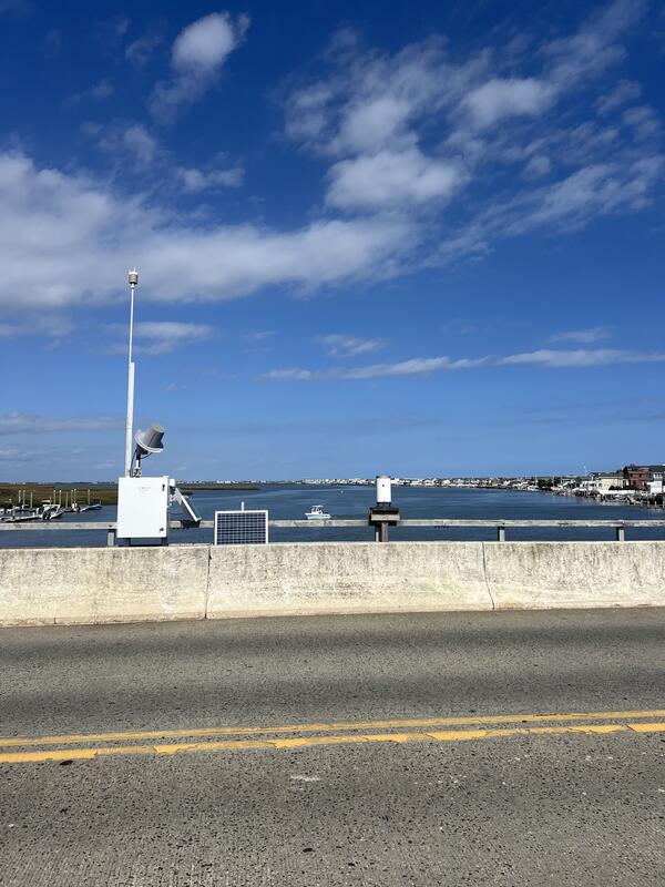 Looking at a box housing a weather sensor and mast and a rain gage next to it as we look out over the bay