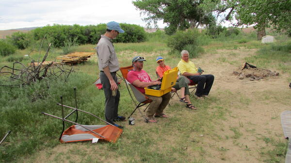 One scientist explaining to other scientists how instrument on his lap works.