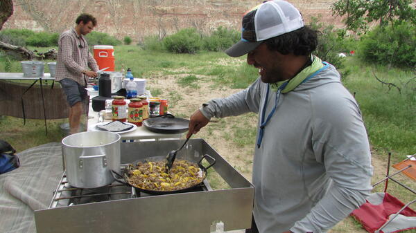 Two guys making dinner at a long table.