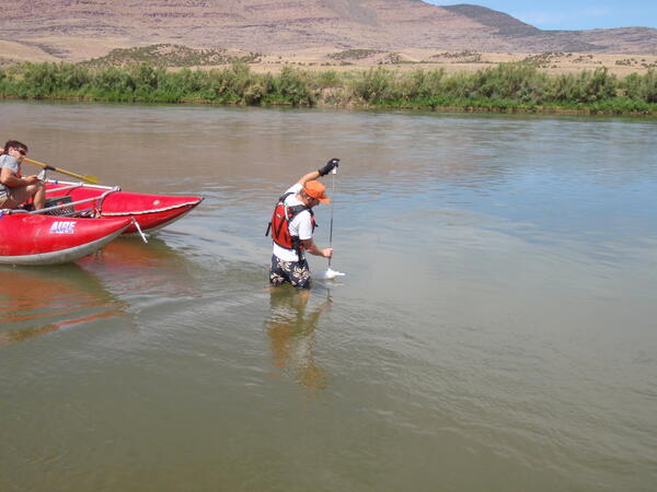 USGS researcher taking a suspended-sediment measurement while wading in knee-high river water