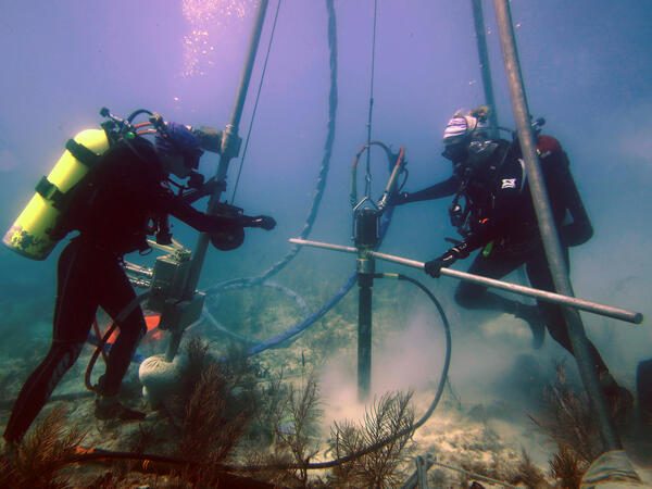 Two divers use a tripod and drill to take a coral core