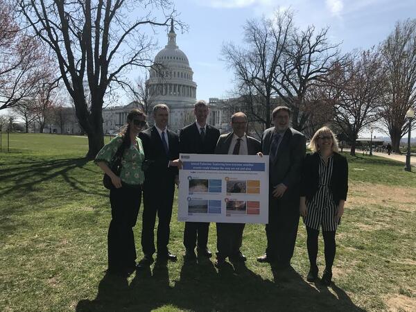 Six USGS Scientists hold up a poster they presented in front of the U.S. Capitol.