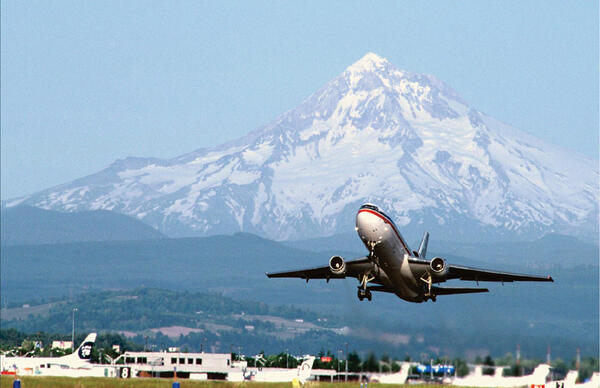 Airplane taking off with snow covered volcano in the background.