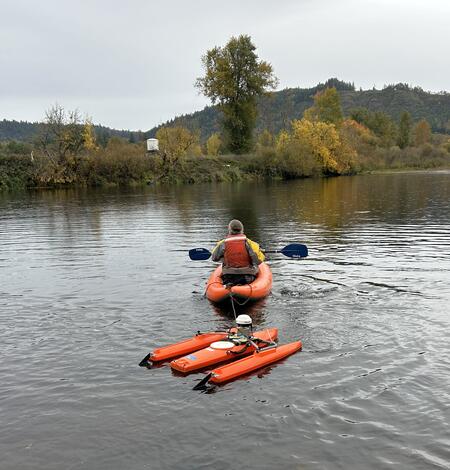 man paddles orange kayak towing an orange boat with flow measurement equipment 
