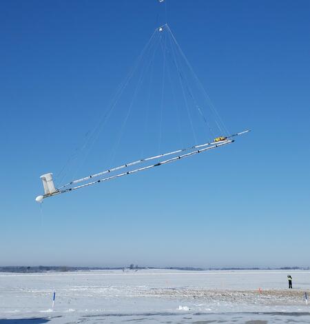 Helicopter with large hoop hanging below, technician on snowy ground for scale