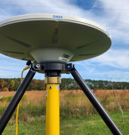 A disc-shaped GNSS receiver mounted atop a gps survey tripod