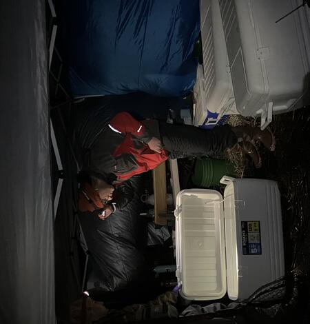 Photo of scientist in red and black jacket out in tent bent over cooler with fish in Klamath Falls, OR