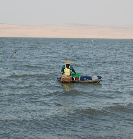 Person pushes a raft with equipment out to equipment in thigh deep choppy water