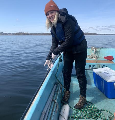 Woman smiling standing on bow of boat holding on to rope to sample water
