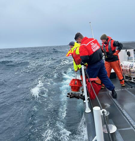 People leaning over side of ship lowering equipment into the water