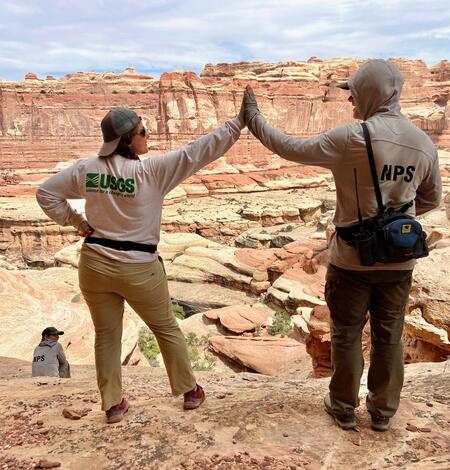 A USGS and NPS scientist give each other a high-five while doing fieldwork