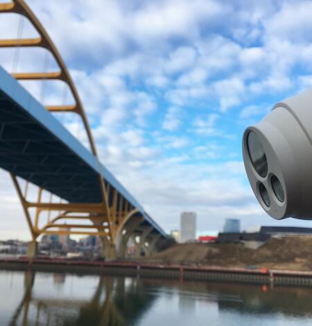 Close up view of webcam pointed towards urban river and bridge in background