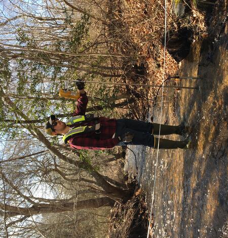 A man stands in a shallow stream with a flow meter.