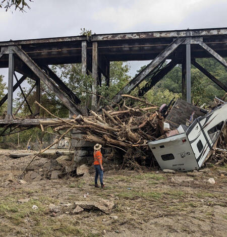 Image shows a large pile of debris left behind after major flooding. A damaged camper can be seen in the pile. 