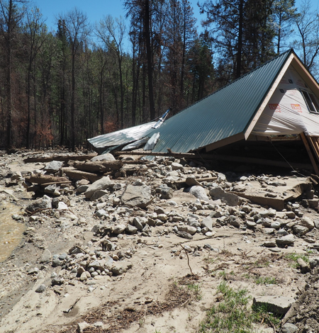 damaged house surrounded by mud, boulders, and tree trunks and branches