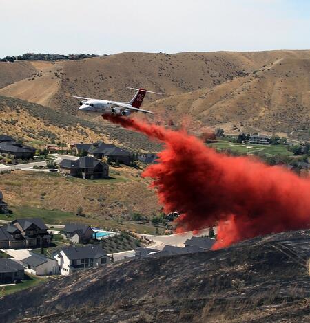 White airplane drops red fire retardant over the hills near a neighborhood