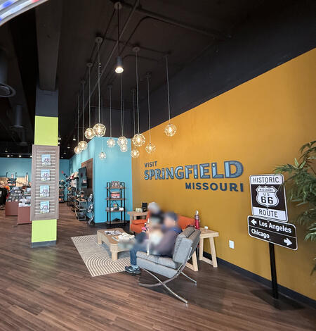 Wide view inside the visitor center, showing seating, merchandise displays, and a wall reading “Visit Springfield Missouri.” 