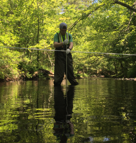 USGS scientist standing in a river collecting a water sample