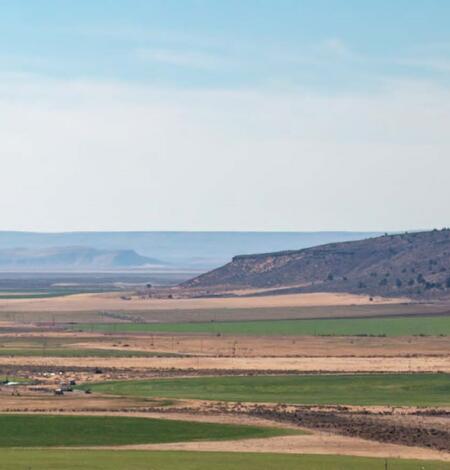 sprawling landscape of green irrigated crop land in between dry yellow vegetation patches on a hazy blue sky day
