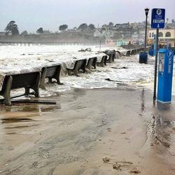 Parking spots and benches near a short seawall at the beach are inundated by winter waves. 