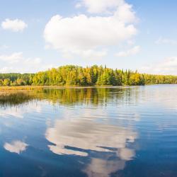 Clear blue lake with green trees in the background and blue sky with clouds reflected in the water