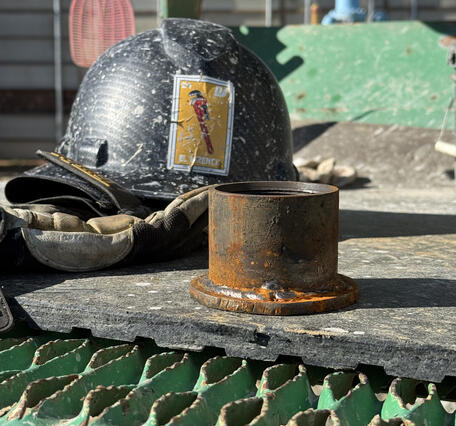 A metal endcap with a flat base which serves at the foot of an extensometer. It is about half the size of a nearby hardhat.
