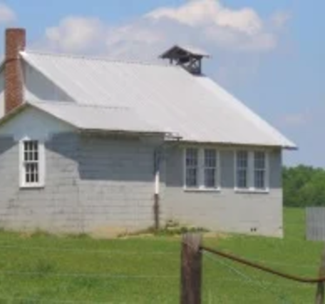 Image from the Amish America website of a simple Amish schoolhouse with white roof, red brick chimney, and an outhouse.