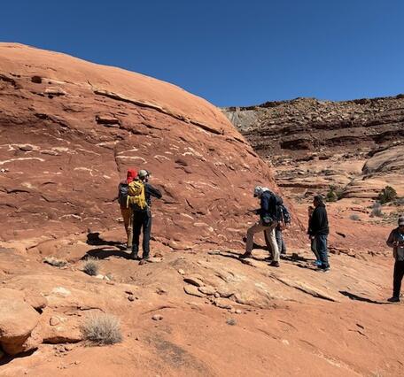 Seven people stand next to a large rock outcrop in the Utah desert. 