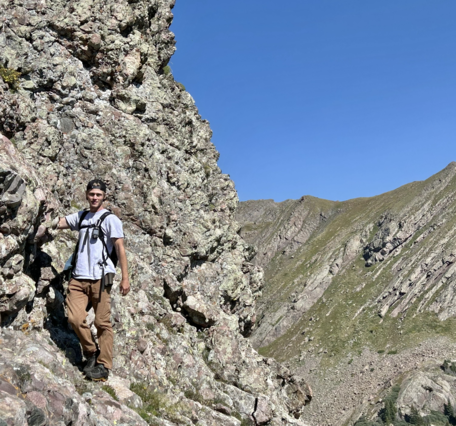 A person is seen standing on the side of a rocky mountain cliff.